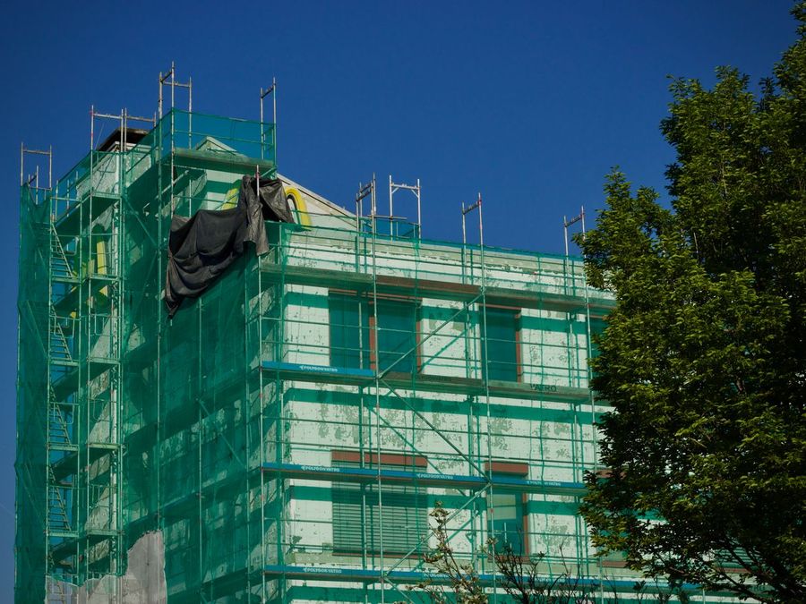 Building wrapped in green scaffold netting against a blue sky